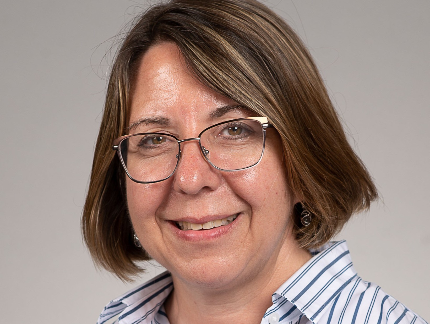 Professional headshot of a middle aged white woman with brown hair and glasses. She is smiling.